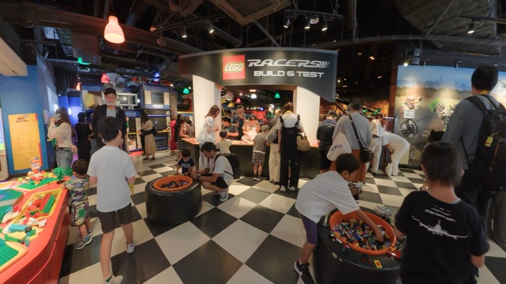 LEGO RACERS BUILD & TESTの看板と、タイヤ型のパーツ入れを囲む子どもたち